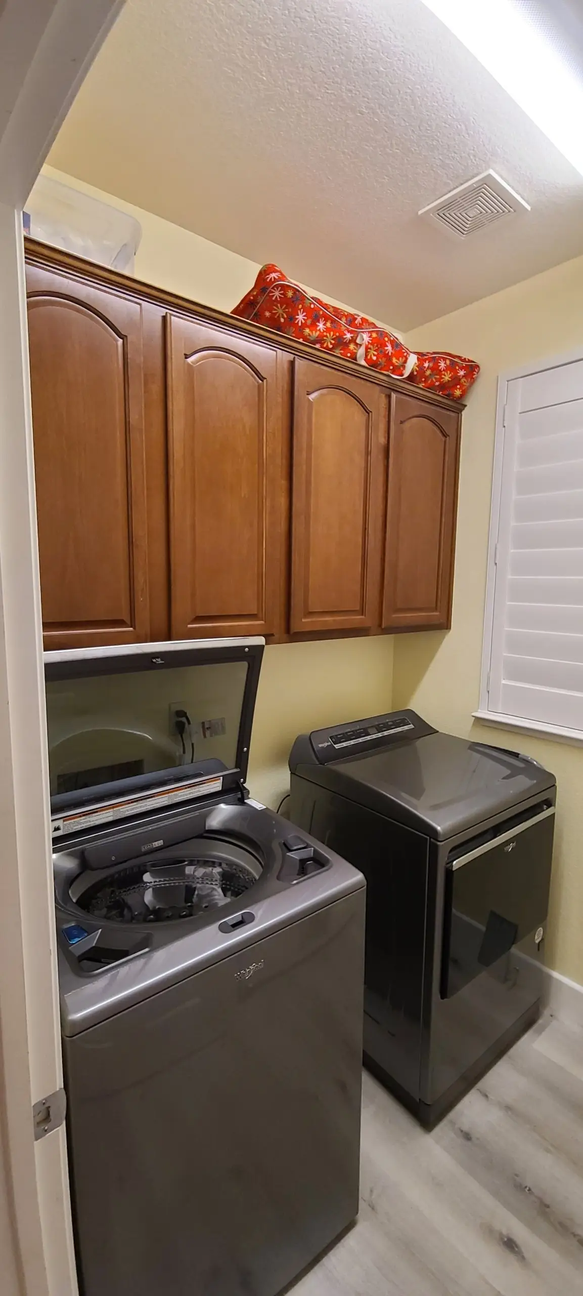 Laundry room with arched-panel, wood-stained upper cabinets above a washer and dryer