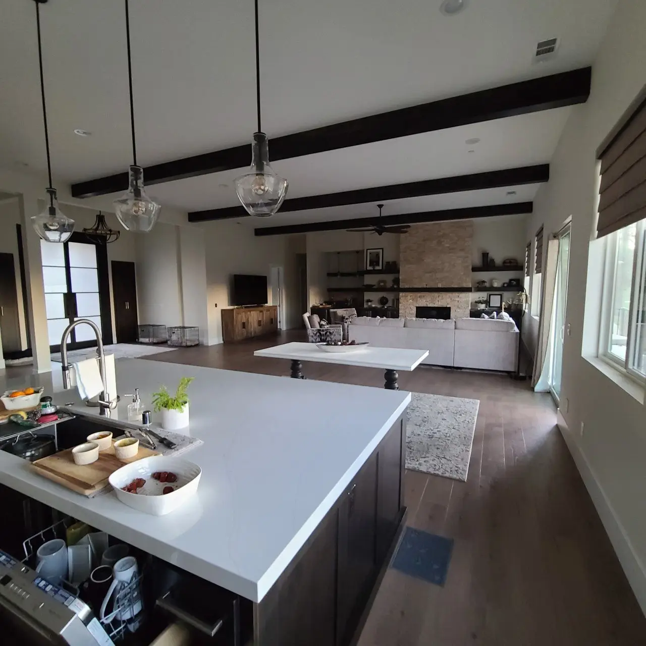 Open-plan kitchen and living room with warm white walls, dark ceiling beams and a stone fireplace