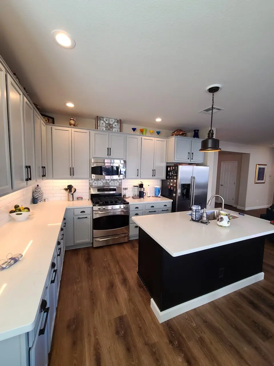 L-shaped kitchen with cabinets painted soft grey, white subway tile and a black-based island