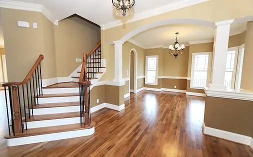 Two-tone painted entryway with tan walls, white trim, arched columns and a curved staircase